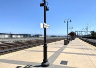 Empty train platform with multiple lengths of track on either side and a large open plot of land behind a fence on the other side of the tracks