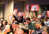 A group of people hold up signs supporting map 5 in a high school auditorium
