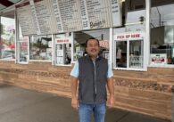 A man standing in front of a walk up burger window in San Jose