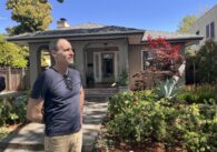 A man standing outside his single-family home on a sunny day