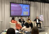 Four people sitting on arm chairs on a raised stage in front of a projected banner introducing "SV@Home's affordable housing month 2024 Housewarming" event