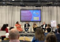 Four people sitting on arm chairs on a raised stage in front of a projected banner introducing "SV@Home's affordable housing month 2024 Housewarming" event
