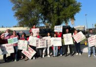 A group of high school teachers stand holding signs calling for better wages