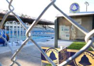 Chain link fence in front of the Santa Clara Swim Club's empty notice board and two large pools with an empty audience stands.