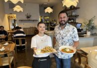 A man and a woman stand facing the camera holding plates of food