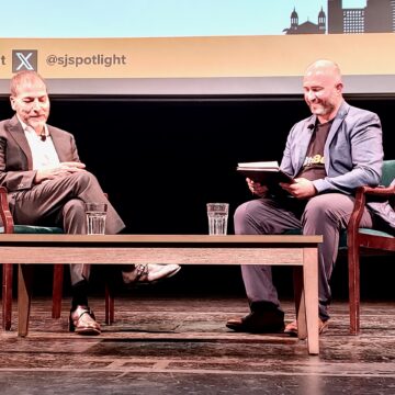 PolitiBeat 2024 Two men sit on a stage in chairs with a table in front of them