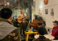 A person plays the guitar to a small audience in a coffee shop