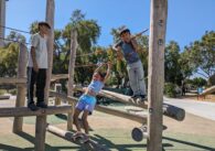 Three children climb on wooden play logs at Emma Prusch Farm Park