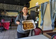 A woman stands in a restaurant holding up a metal tin of uncooked kebab meat