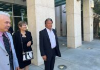 Three people two men and one woman standing next to a building.