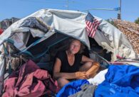 A homeless woman sits in a tent surrounded by her personal items