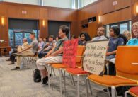 Cupertino residents sit in rows of chairs during City Council, with signs that read "No high rises! No more traffic near Faria School please!" and "Save our single family homes. Don't build 23 units on Scofield Drive! Your neighbor could be next!"