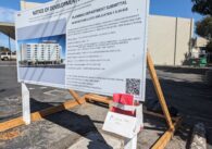 A notice of development proposal sign with a homemade cardboard box holder carrying red flyers attached to the sign.