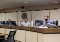 Three men sit behind a dais