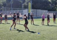 Female high school students practice flag football at Los Gatos High School. One teammate holds her arm back, ready to throw the football.