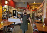 A man in an apron stands inside a restaurant