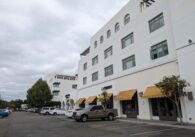 A four-story, white apartment complex building with retail on the bottom floor