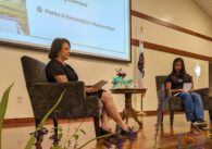 A woman sits on a stage in a velvet chair across from a girl sitting in a velvet chair.