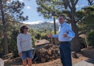 A woman wearing a striped long-sleeve shirt and sunglasses stands next to a man wearing a button-up long-sleeve shirt and jeans in front of the Los Gatos hillside wild.