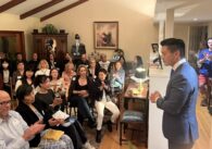 A crowd of supporters listens to a politician talk inside a house party