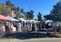 People walk between pop up tents and food vendors at an outdoor community festival