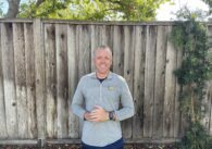 A man standing outside in front of a wooden fence