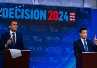 Two men in suits stand on a stage behind podiums