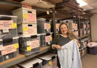 A woman holds sweatpants in a storage room of boxes of clothes