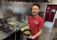 A man holds a bowl of noodles in a kitchen
