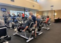 Two older adult men working out at a gym