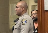 A correctional officer stands in the foreground, with an incarcerated man behind him