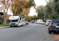 Multiple cars parked along a residential road, with two RVs parked amid the cars