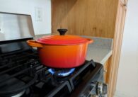An orange pot with a lid sits on a gas flame on a stove.
