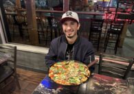 A man sitting inside at a table with a pizza in front of him