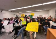 People sitting and holding signs at a school board meeting.