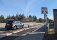 A 30 mph speed limit sign next to a road where cars are driving.