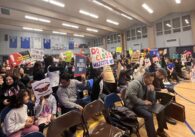 A crowd of people with protest signs at a school board meeting