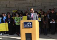 A man stands at a podium with a crowd behind him