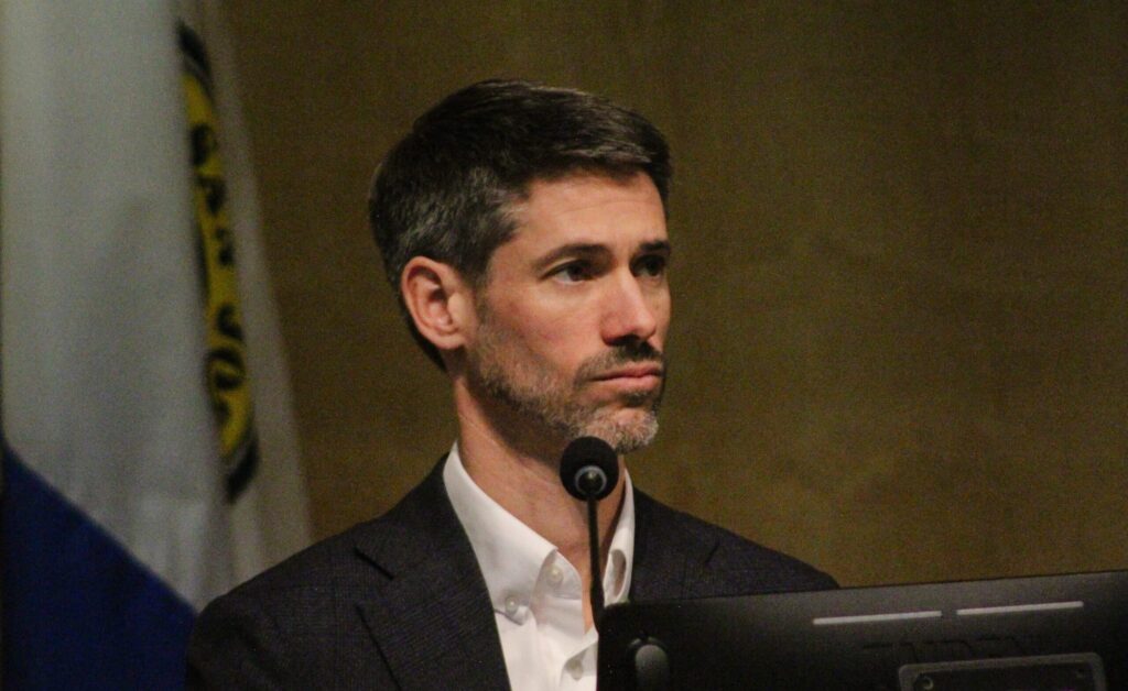 A man sitting behind a microphone and computer at a government meeting in San Jose, California