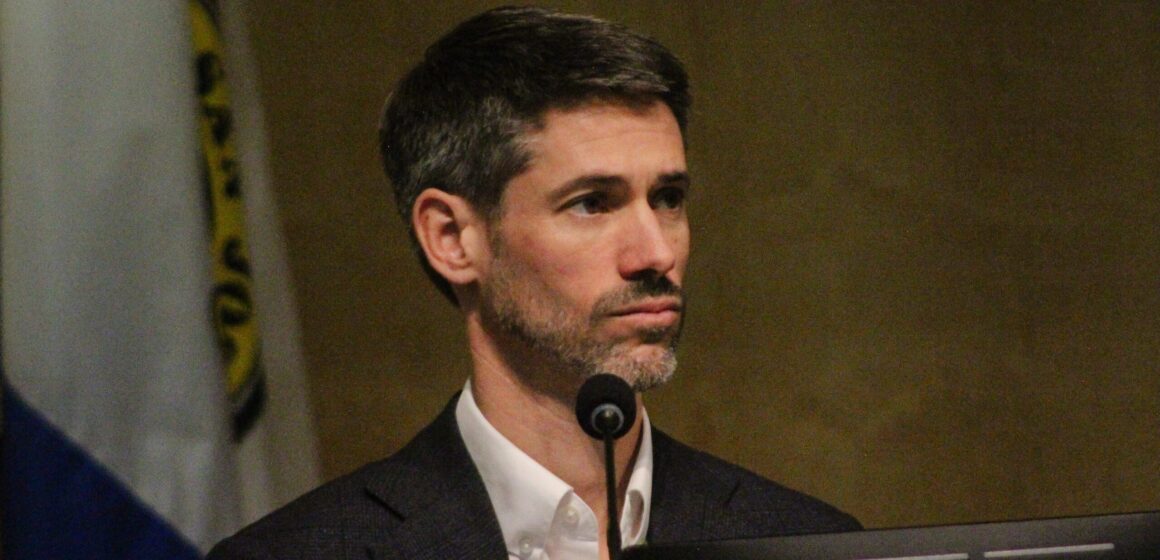 A man sitting behind a microphone and computer at a government meeting in San Jose, California