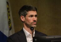 A man sitting behind a microphone and computer at a government meeting in San Jose, California