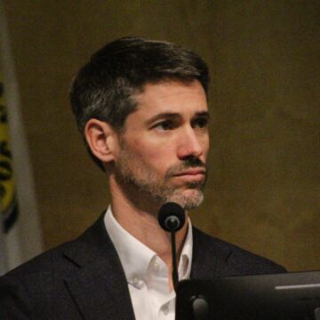 A man sitting behind a microphone and computer at a government meeting in San Jose, California