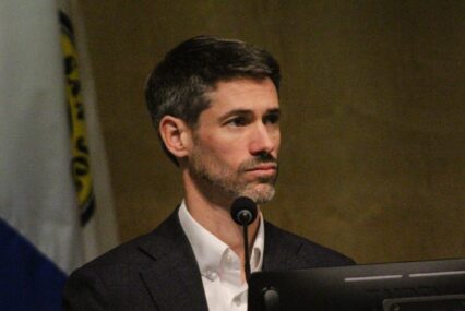 A man sitting behind a microphone and computer at a government meeting in San Jose, California