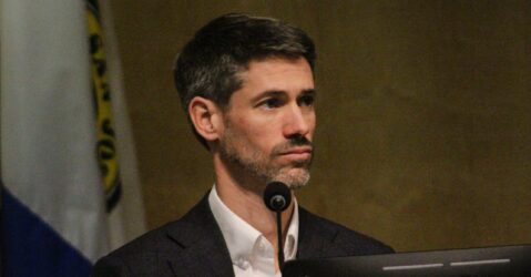A man sitting behind a microphone and computer at a government meeting in San Jose, California