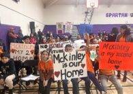 Parents and students hold protest signs at a school board meeting