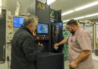 Two men work a manufacturing machine.