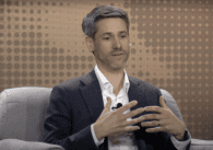 A man gestures with his hands while he speaks on a stage