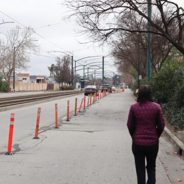 Woman in puffer jacket walks in blocked pedestrian lane while cars drive on the open lanes, with a "share the road" sign above her