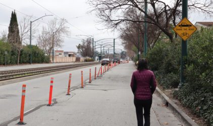 Woman in puffer jacket walks in blocked pedestrian lane while cars drive on the open lanes, with a "share the road" sign above her