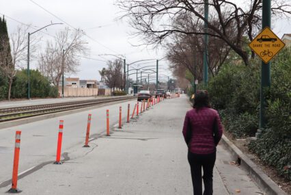 Woman in puffer jacket walks in blocked pedestrian lane while cars drive on the open lanes, with a "share the road" sign above her